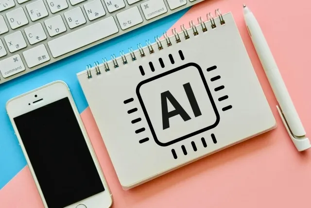ノートに書かれたAIの文字とスマホとボールペンとパソコンキーボード