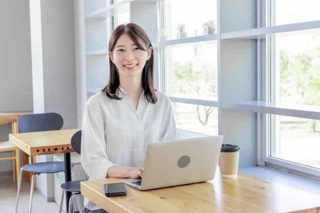 カフェで白いノートパソコンを操作している笑顔の女性