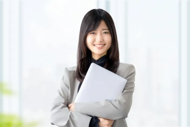 ノートパソコンを胸の前で両手で持ち笑顔の女性