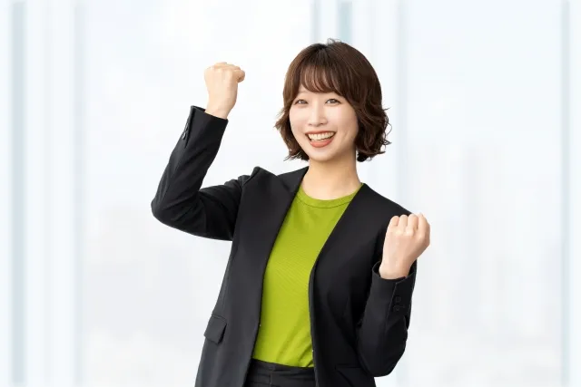 ジャケットを着た女性が右手を上げ気味に両手でガッツポーズしている