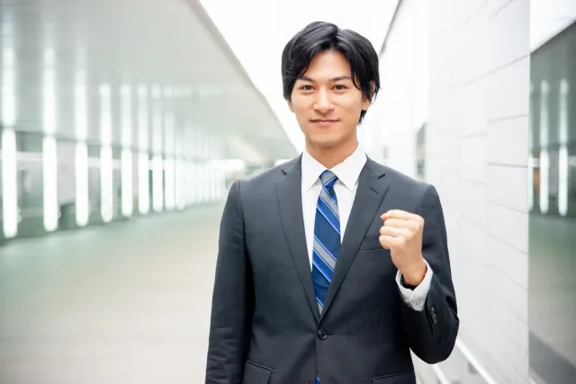 スーツを着て青いチェックのネクタイをした男性が左手でガッツポーズしている