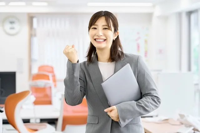 左手でファイルを持ち右手でガッツポーズをするスーツを着た女性