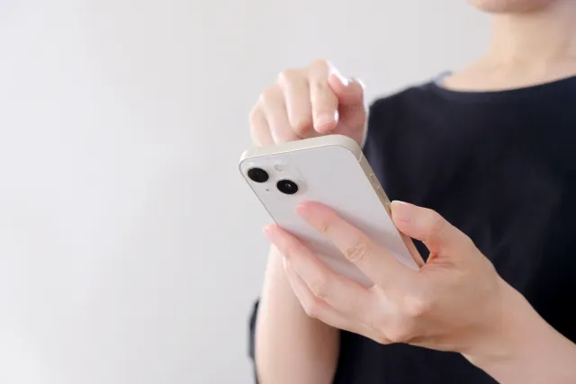 左手でスマホ持ち右手の指で操作する黒い服を着ている女性の手