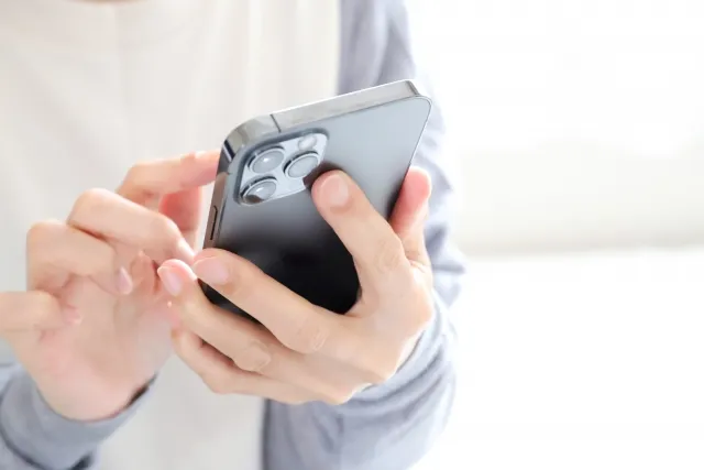 左手で黒色のスマホを持って右手の指で操作する女性の手