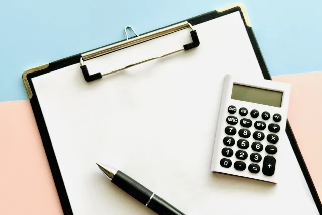 バインダーに挟まれた白紙の紙の上に電卓とボールペンが置かれている
