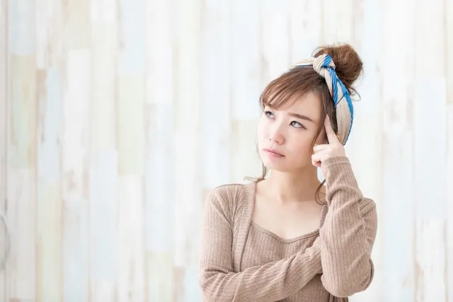 左手の指でこめかみをおさせて考えている女性
