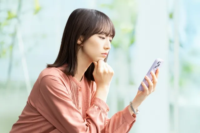 左手でスマホを持ち右手で頬杖するピンクの服の女性