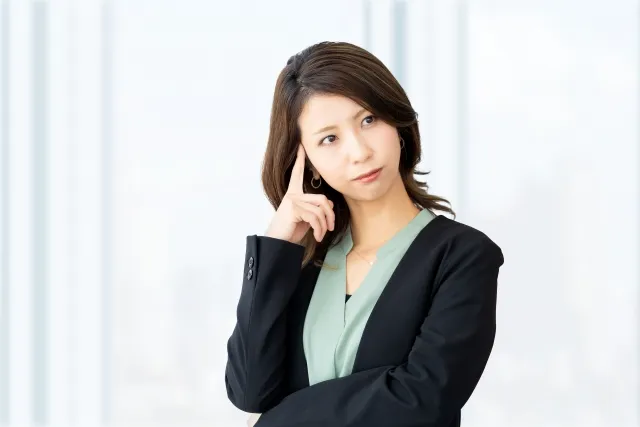 右手の指でこめかみをおさえ考えている黒いジャケットを着た女性