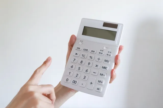左手で白い電卓を持ち右手で操作しようとしている