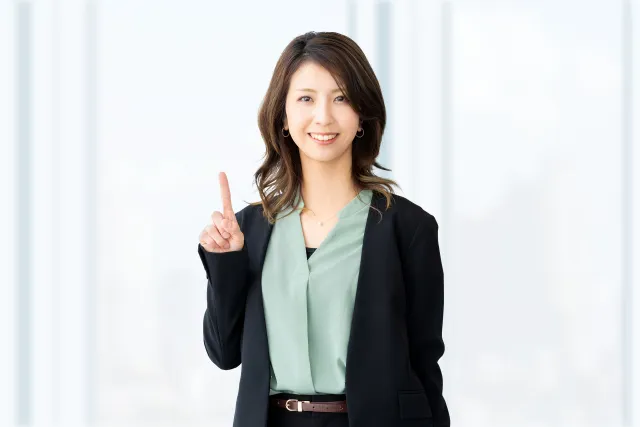 右手の人差し指を上げているオフィスカジュアルの女性