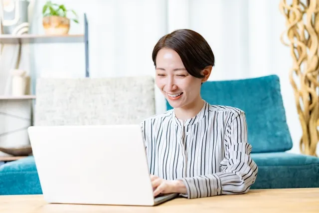 ソファの前に座ってノートパソコンを操作する笑顔の女性
