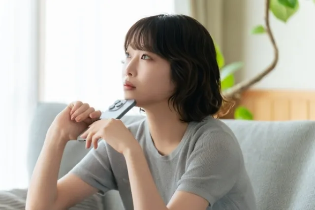 ソファに座ってスマホを両手で持って顎に当てて考えている女性