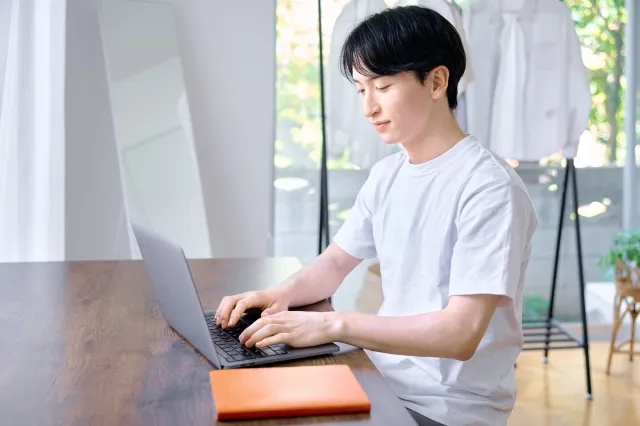 部屋のテーブルでノートパソコンを操作する男性