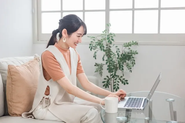 ソファーに座ってテーブルの上でノートパソコンを見ながら笑顔の女性