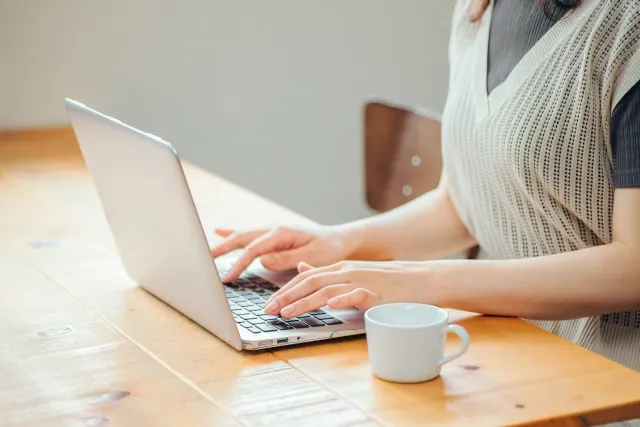 テーブルでノートパソコンを両手で操作している女性の手元