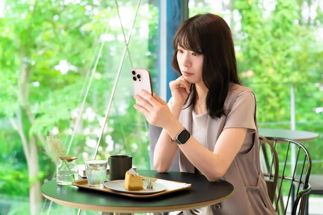 カフェでケーキセットを注文してテーブルに肘を置きながらスマホを見ている女性