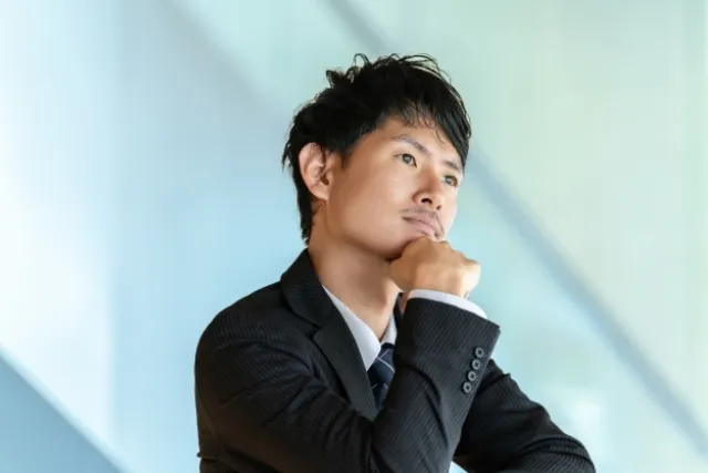 右手で頬杖をつき悩んだ表情をしているスーツを着た男性