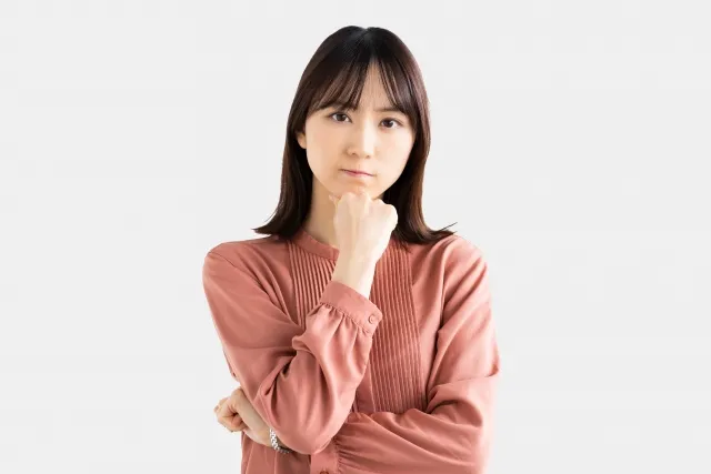 右手で拳を握って顎に当てて考えている表情の女性
