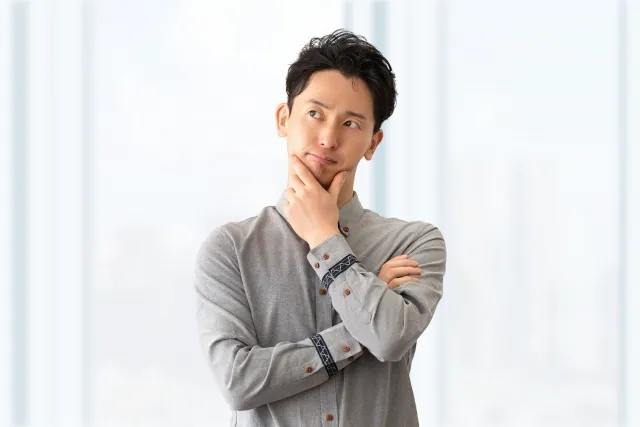 左手で顎を触りながら考え事をしているグレーのYシャツを着た男性
