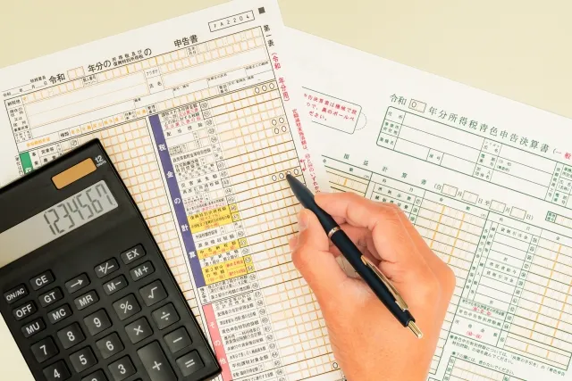 紙の確定申告書に電卓で計算しながらボールペンで記入している様子