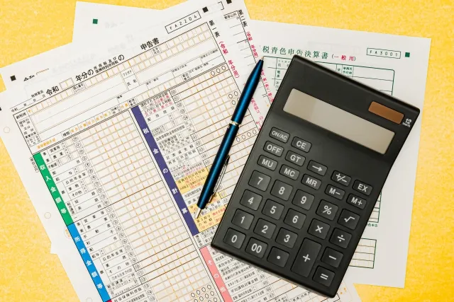 紙の確定申告書の上に電卓とボールペンが置かれている